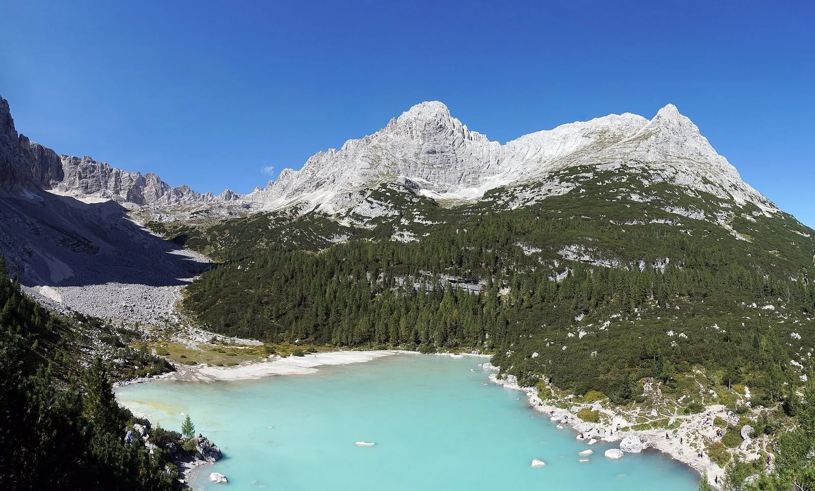 Il Lago di Sorapis con l'acqua turchese, il bosco di conifere e le pareti chiare del gruppo del Sorapiss