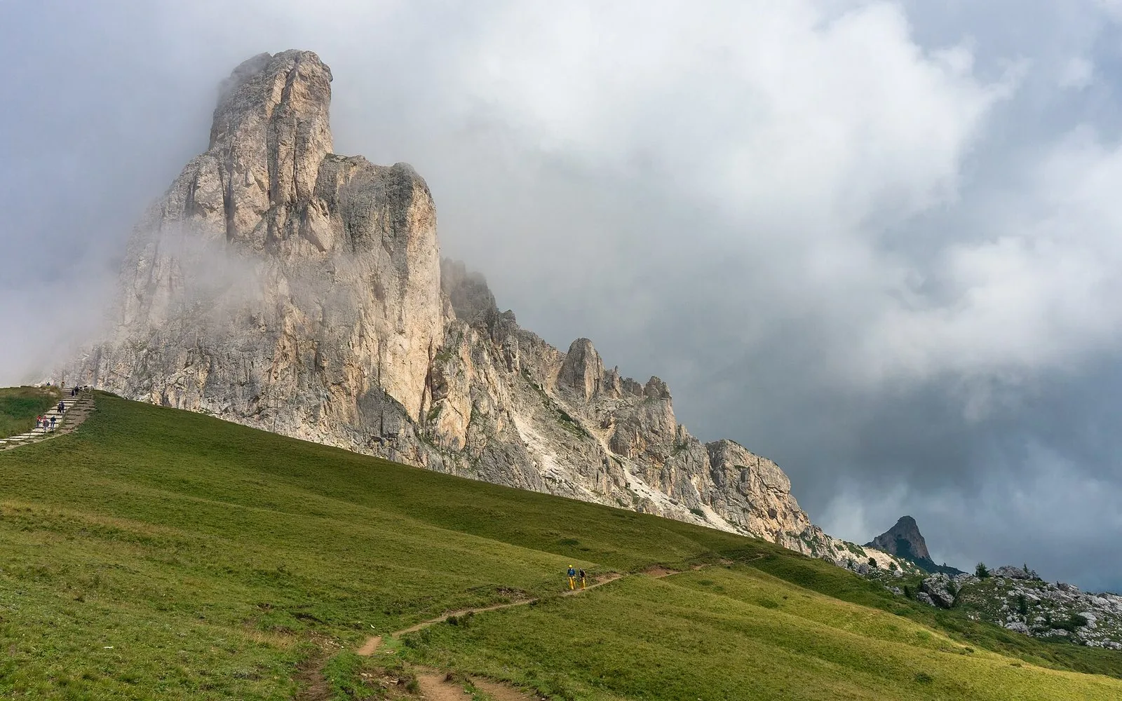 La parete rocciosa di Ra Gusela avvolta dalle nuvole sopra i prati verdi del Passo Giau