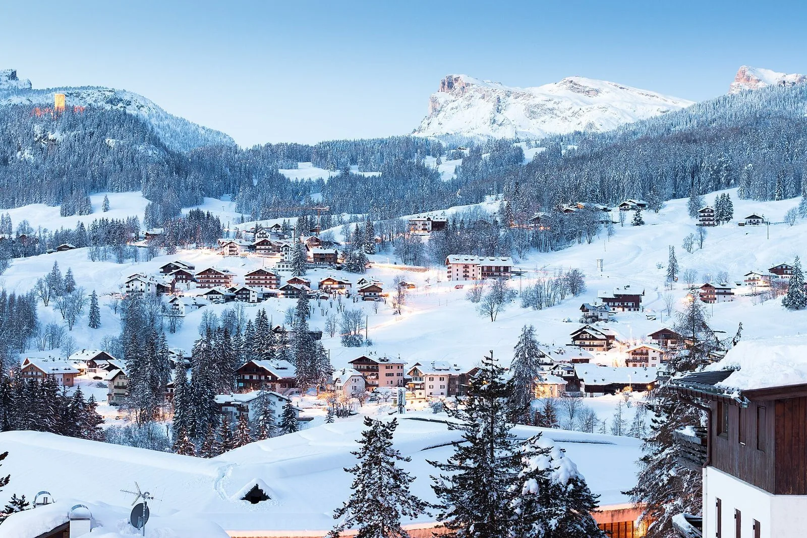 Le frazioni di Cortina d'Ampezzo coperte di neve all'imbrunire, con le luci delle case accese e le Dolomiti sullo sfondo