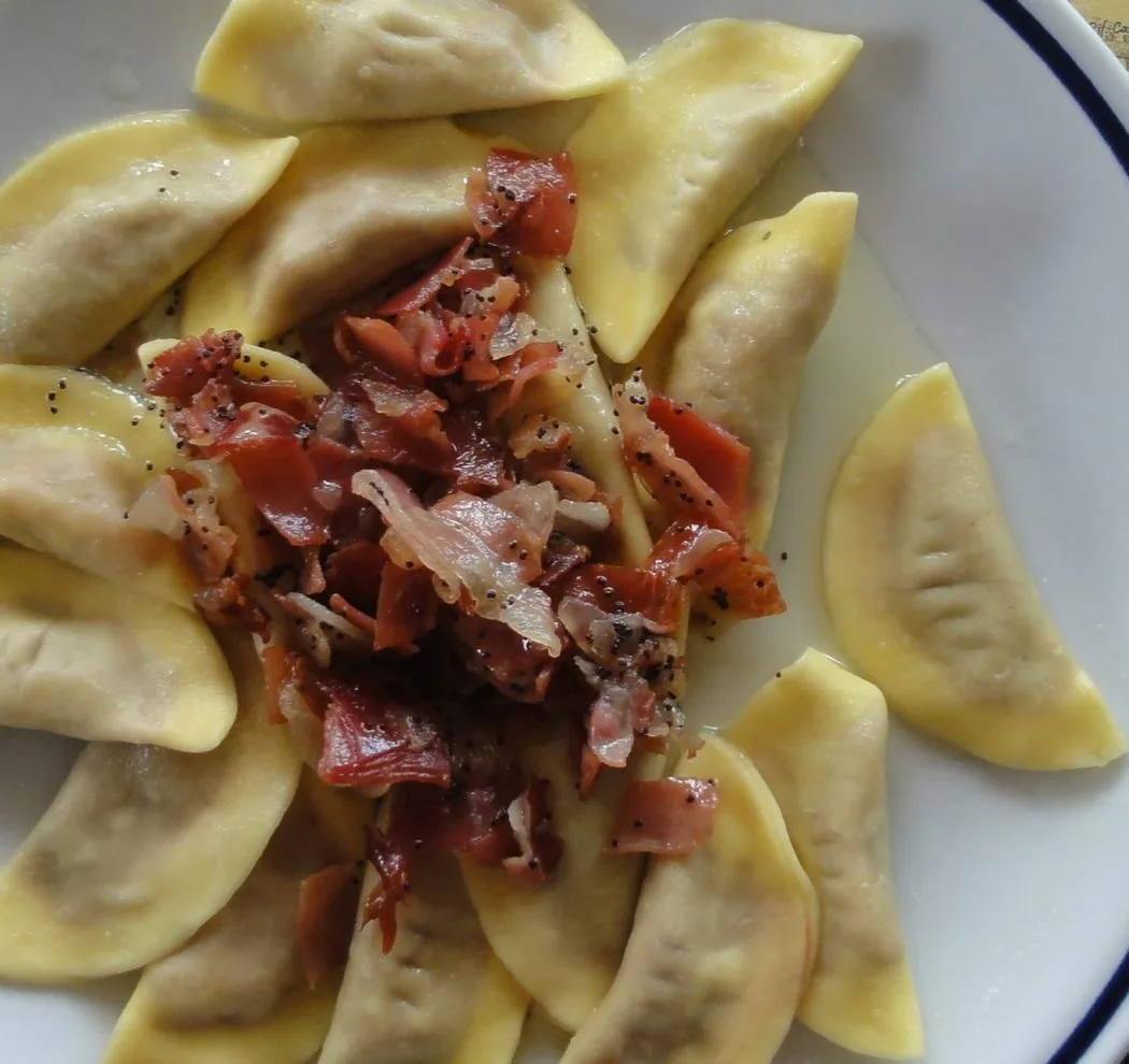 Piatto di casunziei, ravioli a mezzaluna conditi con burro, semi di papavero e speck croccante